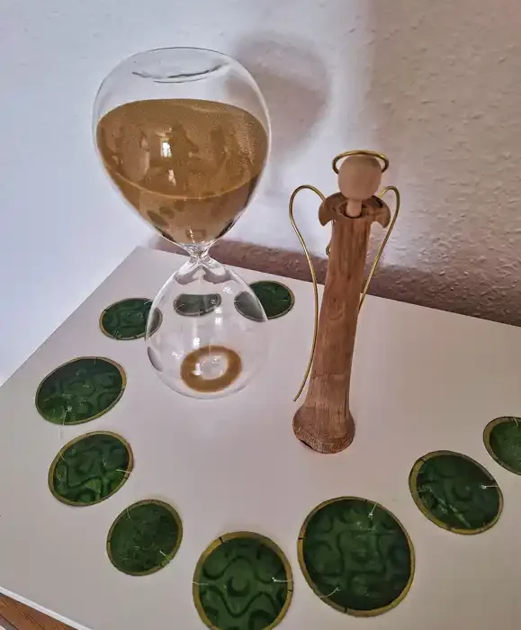 Auf einem weißen Tisch sieht man eine Sanduhr mit einer Holzfigur