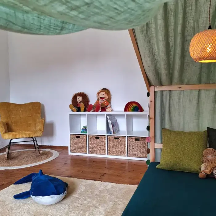 Im Kindertherapieraum ist ein Regal mit Spielzeug, ein Sessel, Ein Himmelbett aus Holz und viele hübsche Stofftiere zu sehen