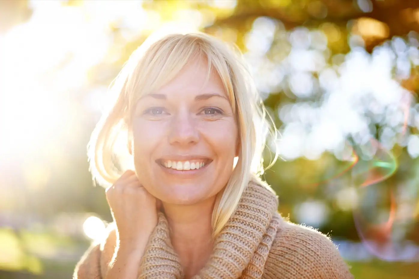 Eine erwachsene blonde Frau schaut in der Abendsonne in der Natur freundlich und sieht glücklich aus, da sie es schafft ihre Angst zu überwinden.