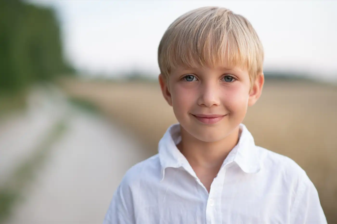 Ein blonder Junge schaut zufrieden mit einem lächeln. Er steht an einem Feldweg. Symbolbild für Kinder